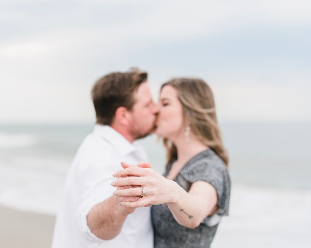 An engaged couple on the ocean front in North Myrtle Beach for their engagement photo, displaying her diamond ring.