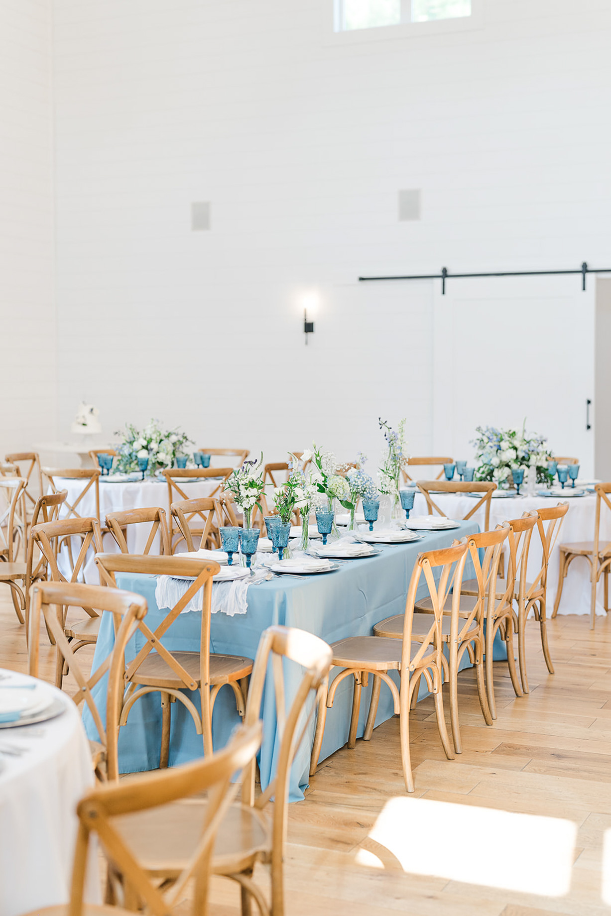 Reception tables set with blue linens, glassware and greenery inside the Main Hall at White Oaks Farm in Myrtle Beach