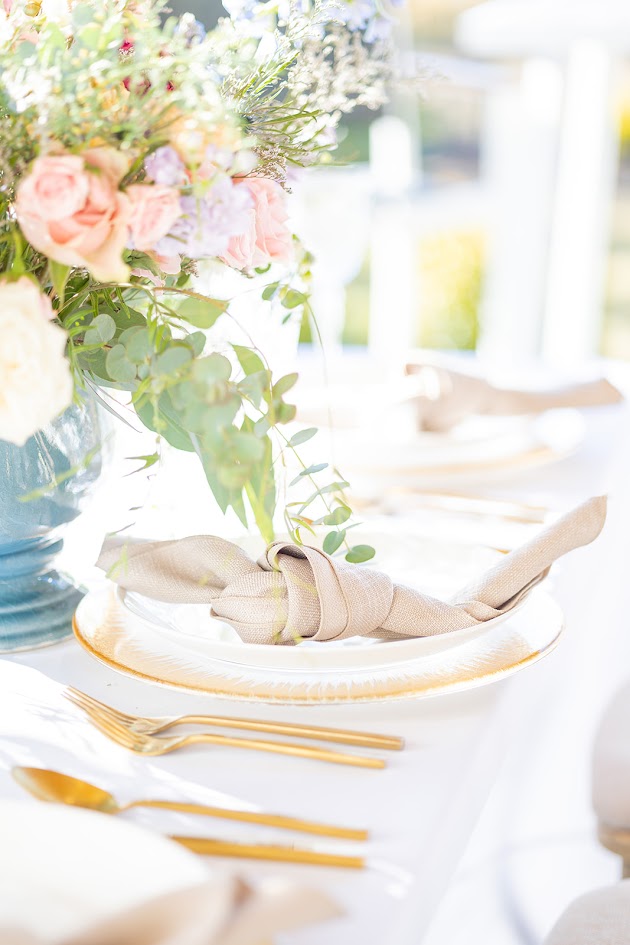 Elegant wedding place setting with fine china, layered dinnerware, pastel napkin, and polished silverware on a decorated table for a luxury Myrtle Beach wedding.