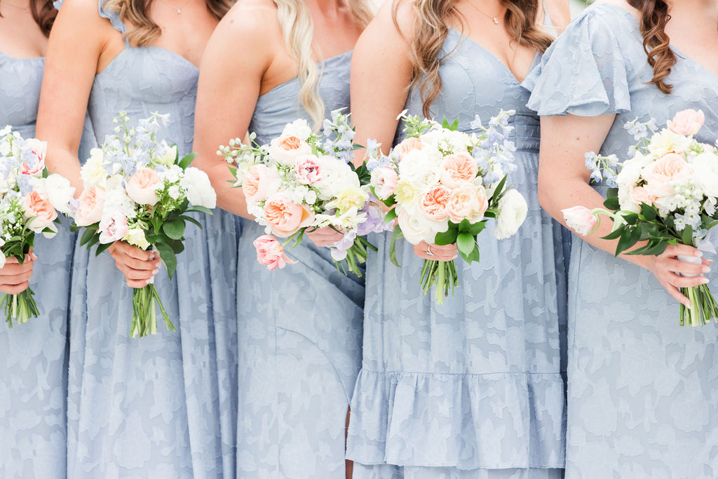 Bridal party portrait with bridesmaids in pale blue bridesmaid dresses holding pastel hued wedding bouquets.