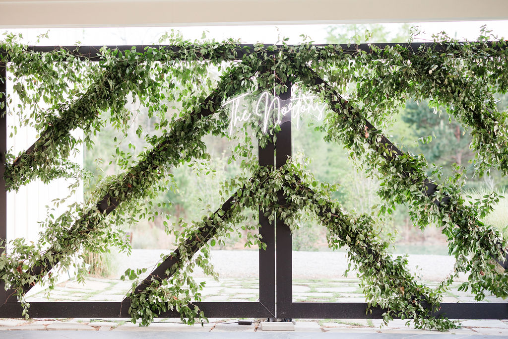 Romantic Myrtle Beach wedding backdrop with greenery-covered steel gates and a custom neon monogram sign highlighting the couple’s style.