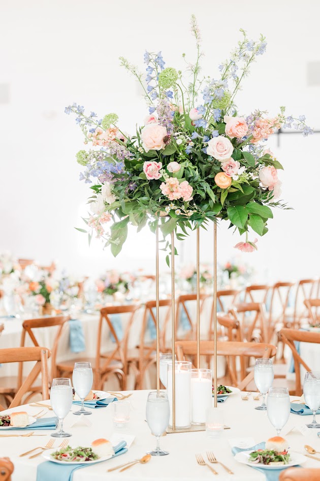 Tall wedding table centerpiece with pastel peach, blush pink, and soft blue flowers, perfect for elegant spring 2026 wedding reception décor inspiration. 