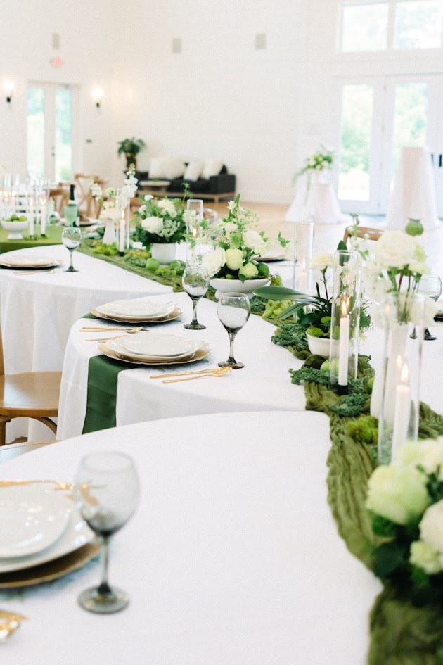 Wedding reception table decorated with shades of green and gold accents, organic florals, and candles at The Venue at White Oaks Farm.