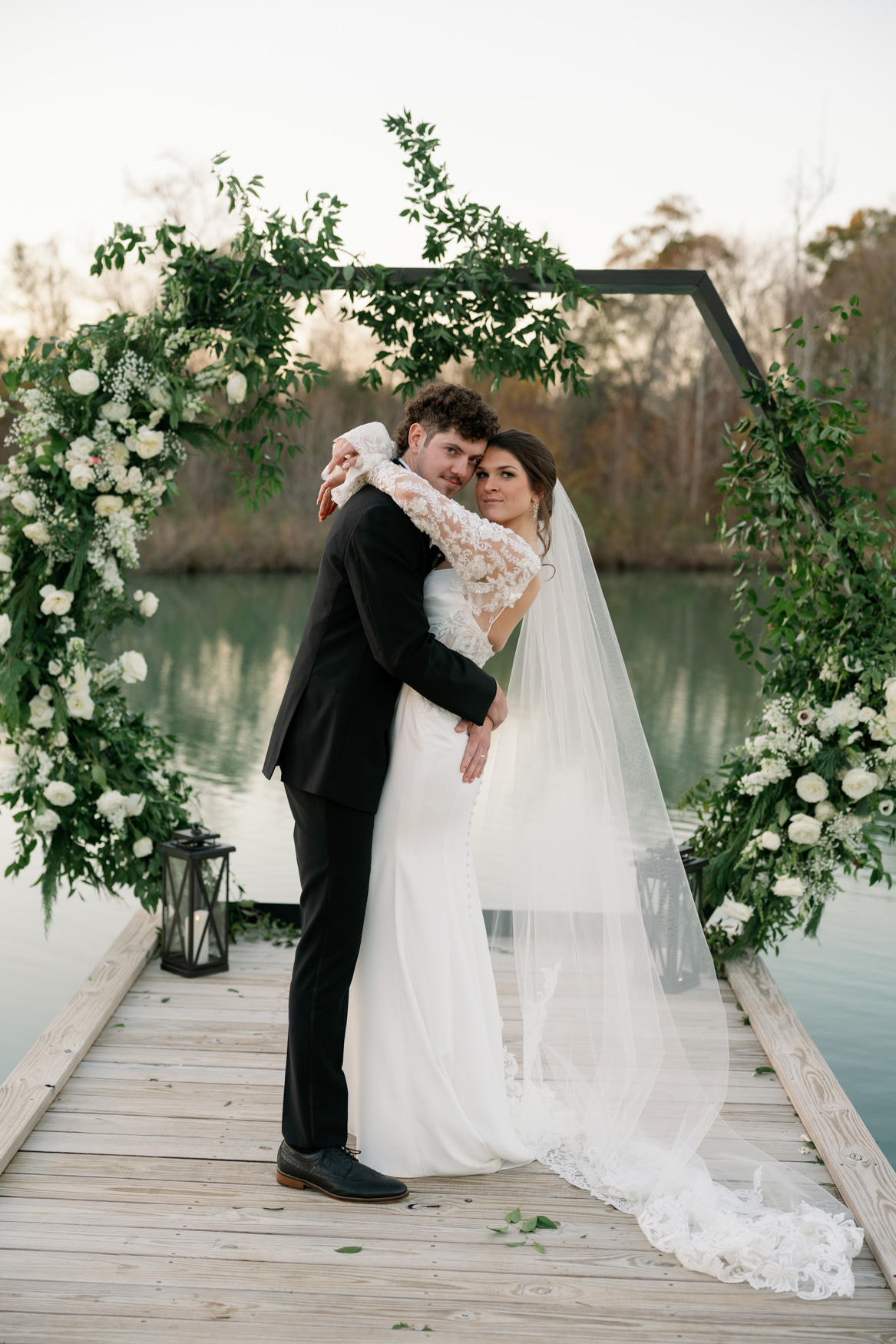 Couple embracing under the flower-covered Hexagon on the dock over the pond at White Oaks Farm